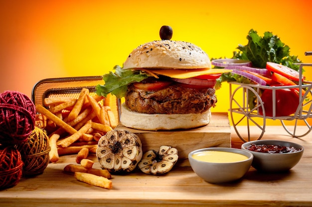 Hamburguesa de queso de ternera con papas fritas, papas y rebanadas de tomate aisladas en tablero de madera, vista deslizante en la mesa, comida rápida