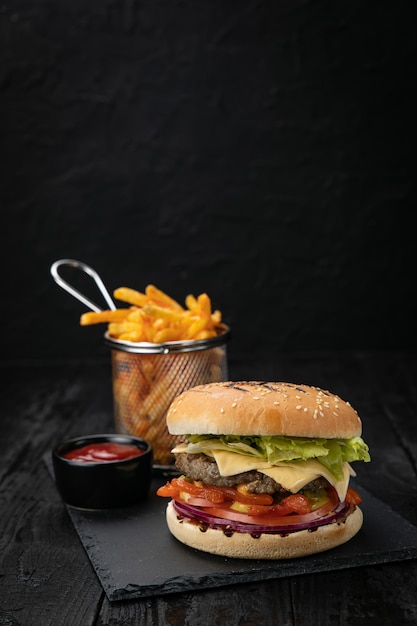 Hamburguesa con salsa y papas fritas en una mesa de madera oscura.