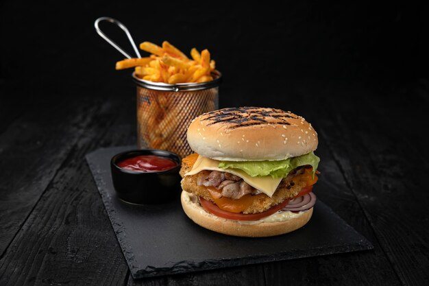 Hamburguesa con salsa y papas fritas en una mesa de madera oscura.