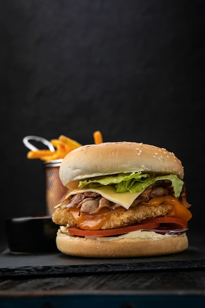 Hamburguesa con salsa y papas fritas en una mesa de madera oscura.