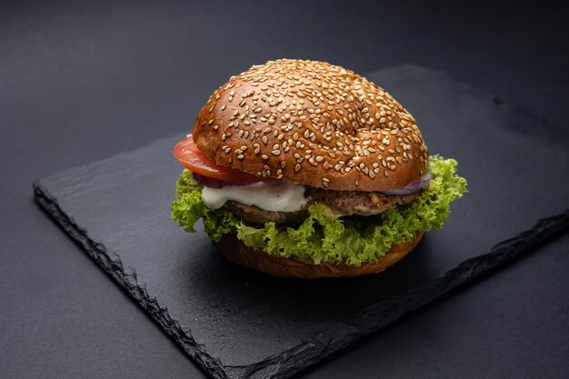 Hamburguesa en un tablero negro sobre un fondo de madera negra