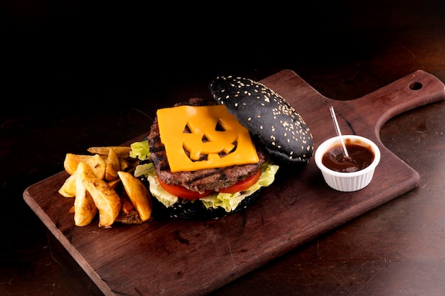 Hamburguesa con temática de Halloween con queso cheddar divertido y bollo negro con gergilin en totora y vista de ángulo de fondo oscuro