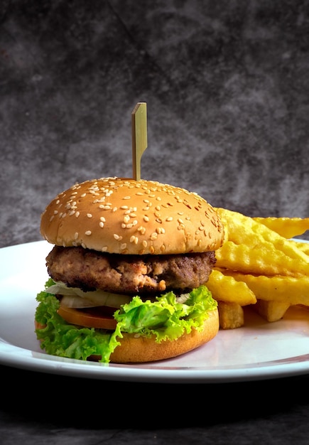 Foto hamburguesa de ternera artesanal y papas fritas sobre fondo negro