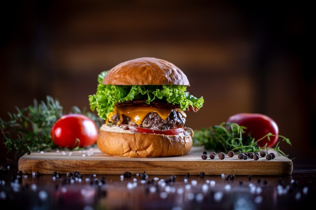 Hamburguesa de ternera artesanal con queso cheddar, tocino, lechuga y salsa sobre fondo de madera