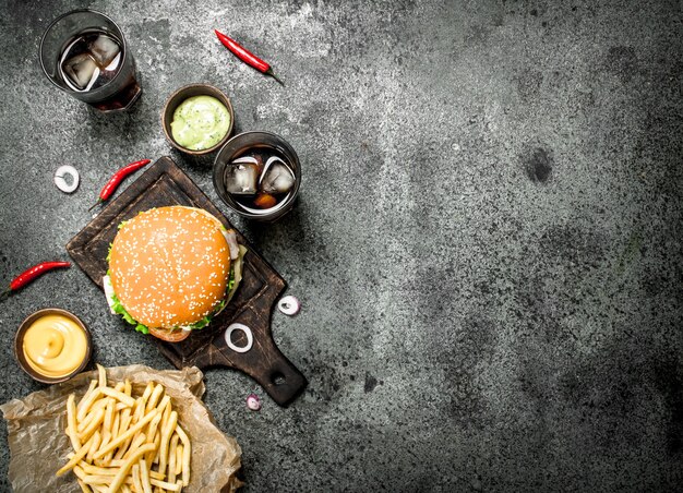 Hamburguesa de ternera fresca con cola y papas fritas. Sobre un fondo rústico.