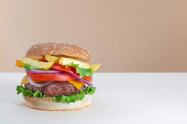 Hamburguesa de ternera jugosa fresca con papas fritas colocadas sobre un fondo de moda creativo beige y marrón