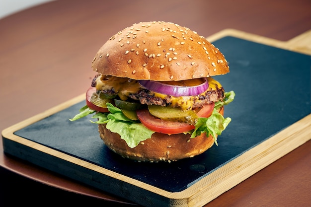 Hamburguesa de ternera con queso, tomate, cebolla en una pizarra. Comida rápida