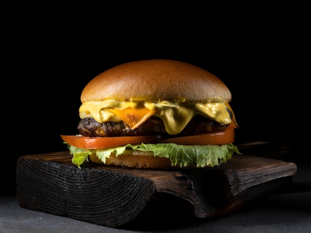 Hamburguesa con tomate de carne de tocino y lechuga sobre tabla de madera y fondo negro Cerrar