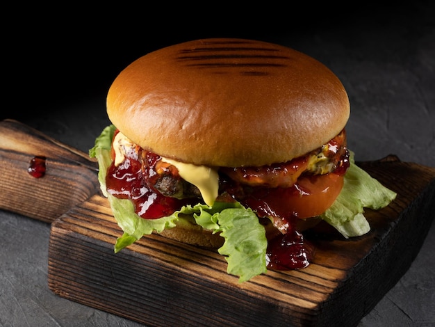 Hamburguesa con tomate de carne de tocino y lechuga sobre tabla de madera y fondo negro Cerrar