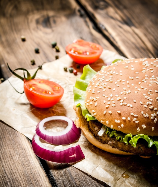 Una hamburguesa con tomates frescos, cebollas y especias. Sobre mesa de madera.