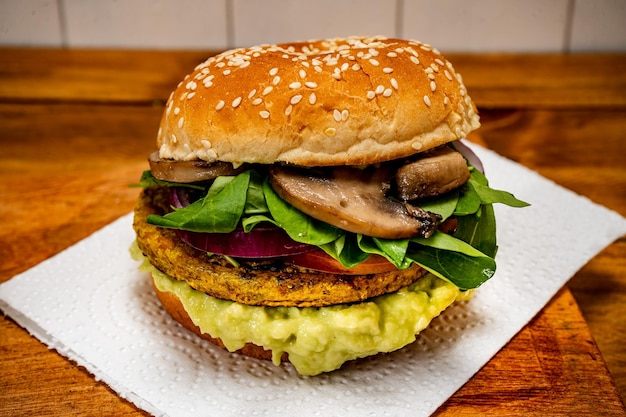 Hamburguesa vegana de proteína vegetal con rúcula de tomate, cebolla roja, champiñones y mayonesa de aguacate sobre una tabla de madera y fondo blanco Vista picada Copiar texto