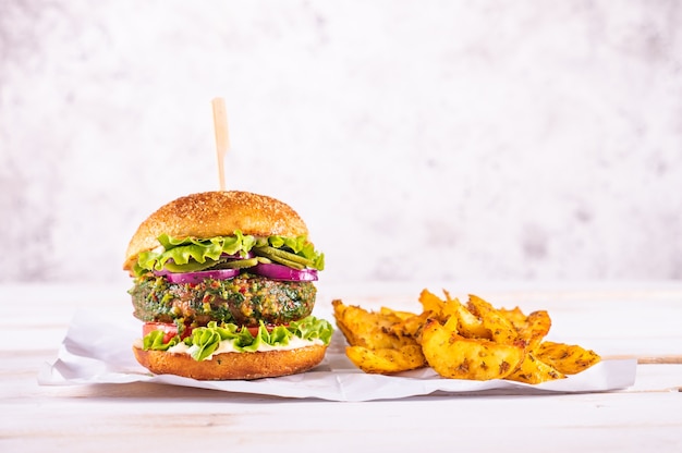 Hamburguesa vegana con rodajas de patata sobre una mesa blanca