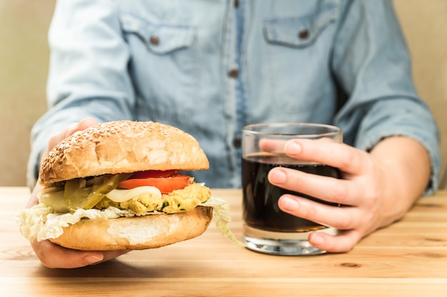 Hamburguesa vegana y vaso de refresco en las manos