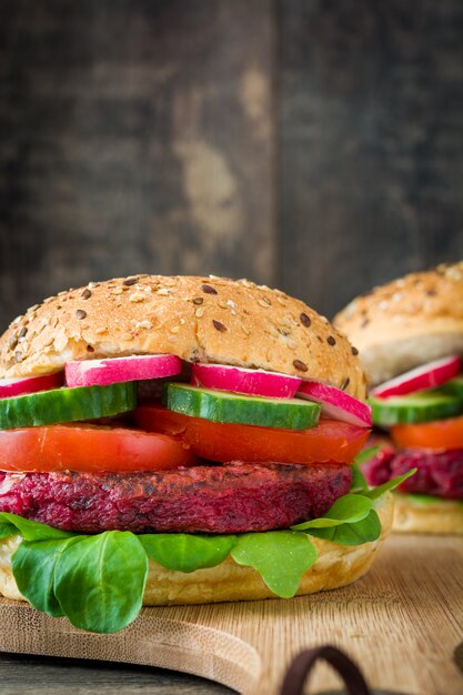 Hamburguesa vegetariana de remolacha con lechuga de cordero, tomate, rábano y pepino en rústica mesa de madera