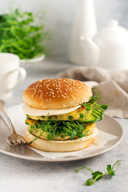 Hamburguesa vegetariana saludable con huevo y brotes de guisantes y semillas microgreen, ensalada fresca, rodaja de pepino sobre una tabla de madera para cortar sobre fondo claro. Enfoque selectivo