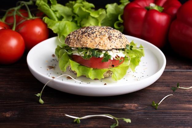 Hamburguesa vegetariana con verduras verdes, rojas y micro sonrisas en un plato blanco sobre una mesa de madera oscura, de cerca.