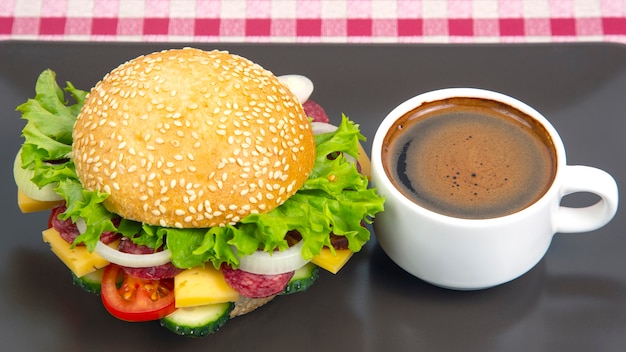 Hamburguesa con verduras y salchicha y café sobre un fondo gris. Comida rápida y desayuno. Calorías y dieta.