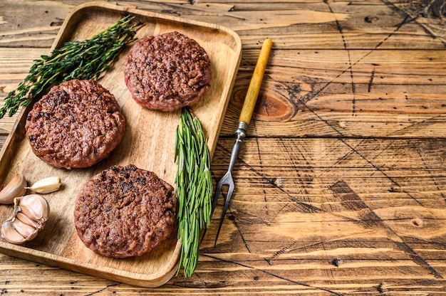 Hamburguesas de bistec de carne molida a la parrilla a la parrilla, carne picada en una bandeja de madera. fondo de madera. Vista superior. Copie el espacio.