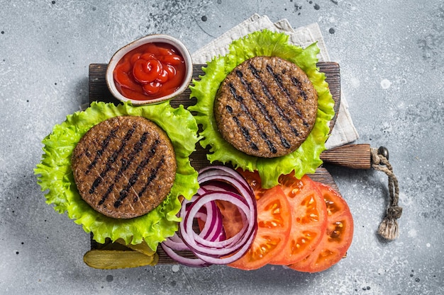 Hamburguesas sin carne a base de plantas con tomate vegano a la parrilla y cebolla en una tabla de servir de madera Fondo gris Vista superior