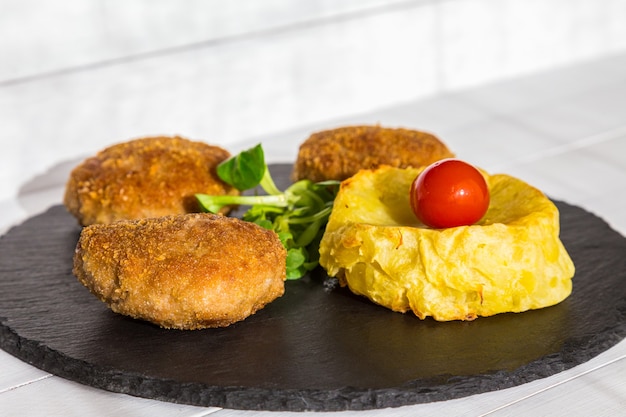 Hamburguesas caseras o chuletas con patatas al horno y ensalada en placa de piedra y mesa de madera.