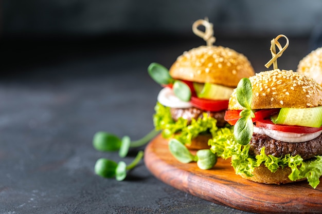 Hamburguesas con chuleta de carne, lechuga fresca, tomates, cebollas en una piedra oscura.