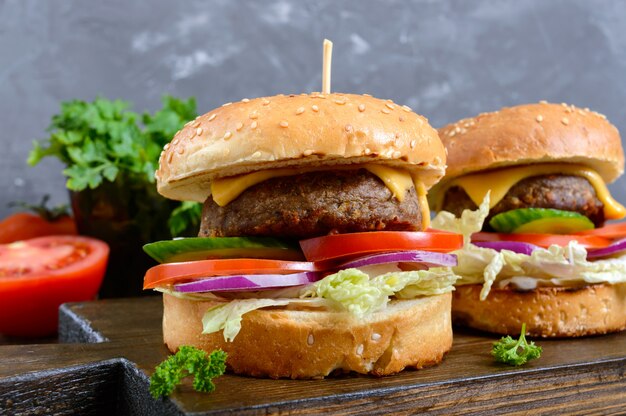 Hamburguesas con chuleta jugosa, verduras frescas, pan crujiente con semillas de sésamo en una mesa de madera. De cerca. Comida rápida tradicional