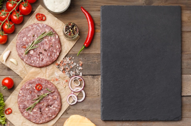 Foto hamburguesas crudas especias verduras placa de piedra con espacio para texto en fondo de madera