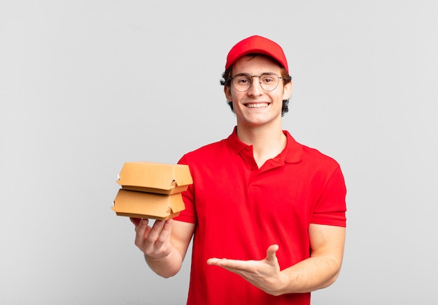Las hamburguesas entregan al niño sonriendo alegremente, sintiéndose feliz y mostrando un concepto en el espacio de la copia con la palma de la mano