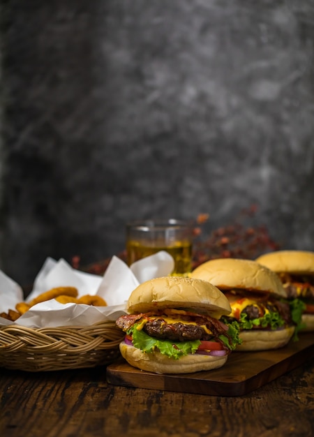 Hamburguesas de ternera con cebollas fritas, espinacas, salsa de tomate, pimiento y queso servido en una tabla de madera con cerveza en el fondo del desván con espacio de copia.