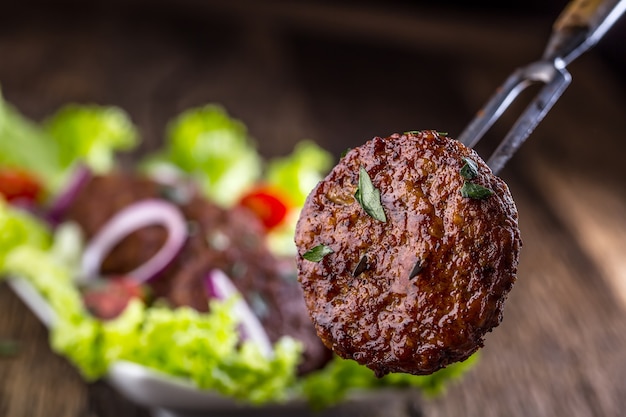 Hamburguesas de ternera chuletas de albóndigas con ensalada de lechuga tomate cebolla sobre tabla de madera.