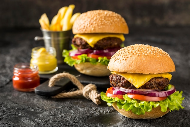 Foto hamburguesas de ternera en tabla de cortar con papas fritas y salsa