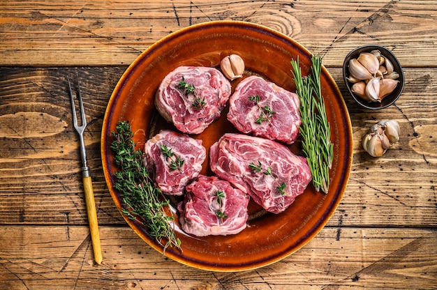 Hammelfleisch vom Lammhals auf einem rustikalen Teller mit Thymian und Rosmarin. hölzerner Hintergrund. Ansicht von oben.