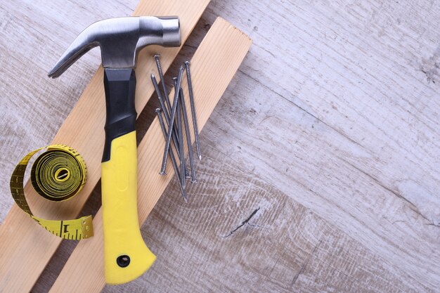 Hammereisen, Zentimeterband und Nägel auf Holztisch