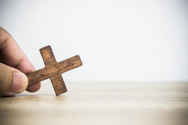 Han hält ein Holzkreuz auf einem Holztisch mit weißer Wand