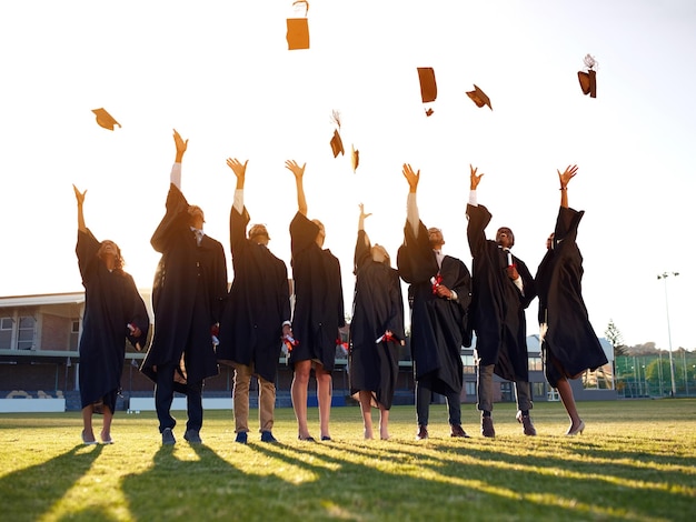 Han llegado al final de sus años académicos Toma de un grupo de estudiantes universitarios lanzando sus sombreros al aire el día de la graduación