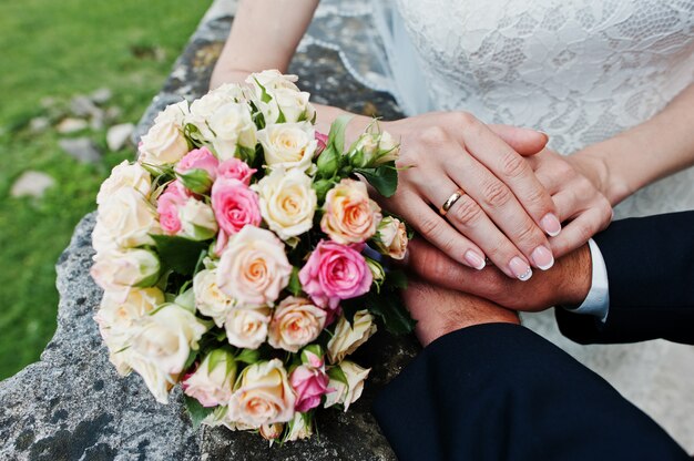 Hand an Hand von Hochzeitspaaren nahe Hochzeitsblumenstrauß.