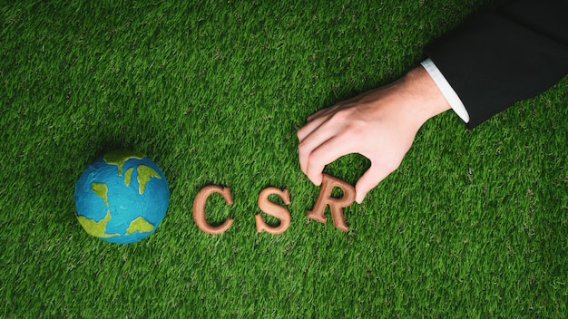 Hand angeordneter Holz-Alphabet-Text in CSR auf biophilem Hintergrund Gyre