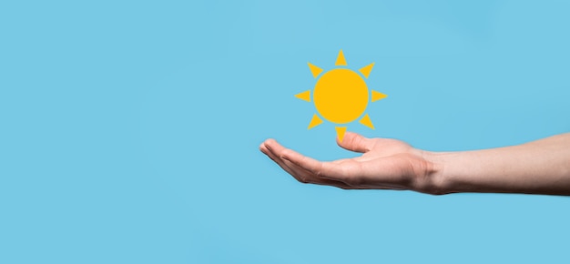 Hand auf blauem hintergrund hält sonnensymbol. nachhaltige stromquelle, stromversorgungskonzept