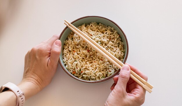 Hand benutzt Stäbchen, um leckere Nudeln mit Dampf auf weißem Hintergrund zu sammeln. Selektiver Fokus. Top-View. Asiatische Mahlzeit auf einem Tisch. Junkfood-Konzept.