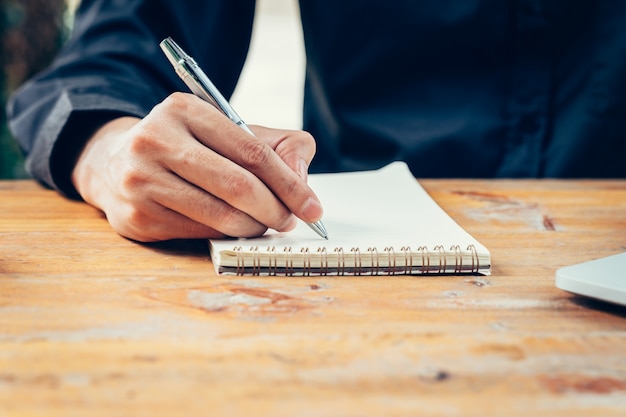 Hand Business Mann schriftlich Notebook auf Holz Tisch im Café.