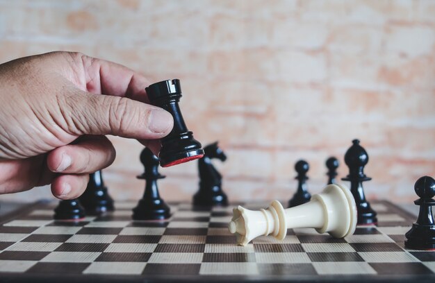 Hand der beweglichen Schachfigur des Geschäftsmannes, zum des Wettbewerbsspiels zu gewinnen