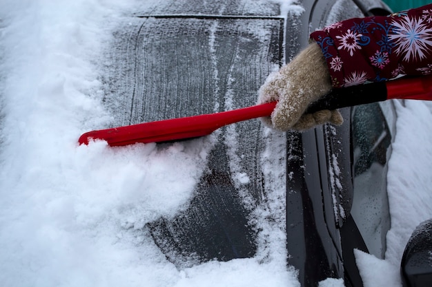 Hand der Frau, die Bürste verwendet und Schnee und Eis vom Auto- und Windschutzscheibenkonzept des Transports entfernt...