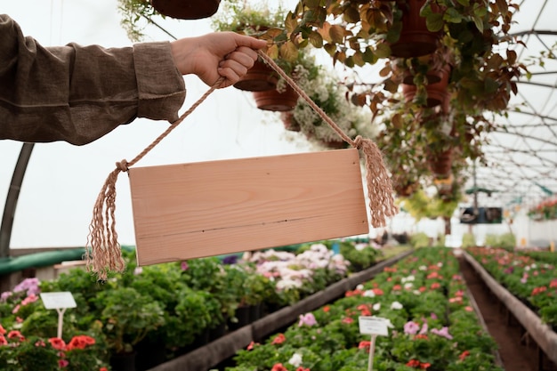 Hand der Frau, die leeres Holzschild im Gartenmall und im Gewächshaus mit Platz für Text hält