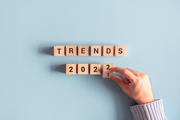 Hand der Frau dreht Holzklötze um und ändert die Trends 2021 in Trends 2022