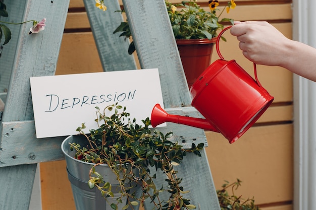 Hand der jungen Frau mit Gießkanne, die Blume und Teller mit Wort Depression gießt.