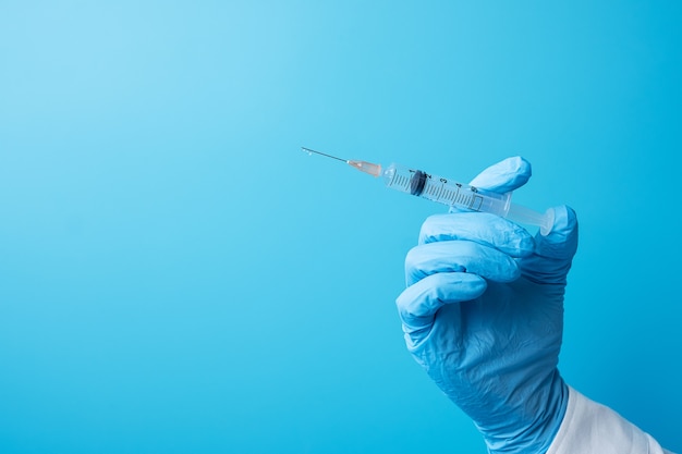 Hand des Arztinjektionsimpfstoffs oder der Droge durch Nadelspritze auf blauem Hintergrund.