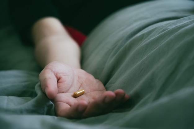 Hand des asiatischen asiatischen Mannes, der Pillen in seine Hand gießt und auf dem Bett schläft