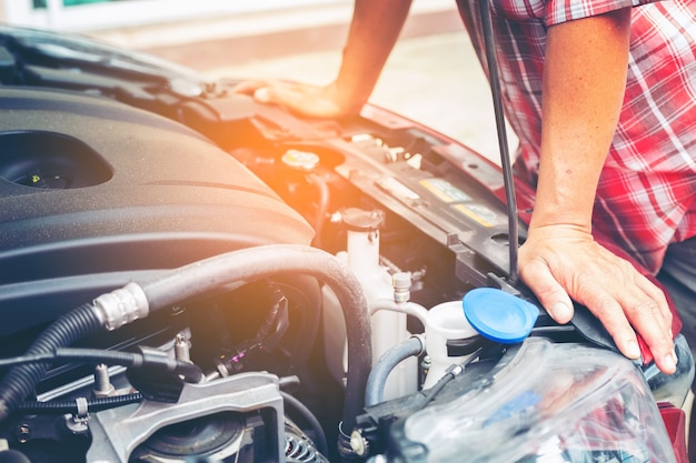 Hand des Automechanikers mit einem Schlüssel. Autoreparaturmechaniker, der Automotor im Autoservice überprüft.