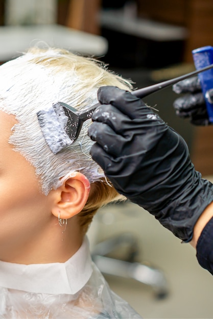 Hand des Friseurs, der weiße Farbe auf das Haar des Kunden aufträgt