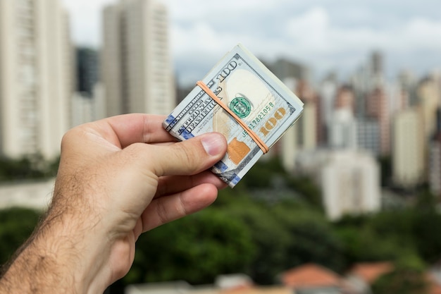 Hand des Mannes, der Dollarnoten vor einer Stadtlandschaft hält